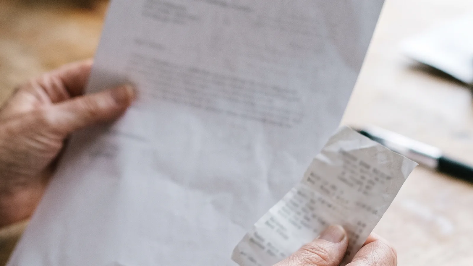 Manos que sujetan una carta y un recibo sobre una mesa